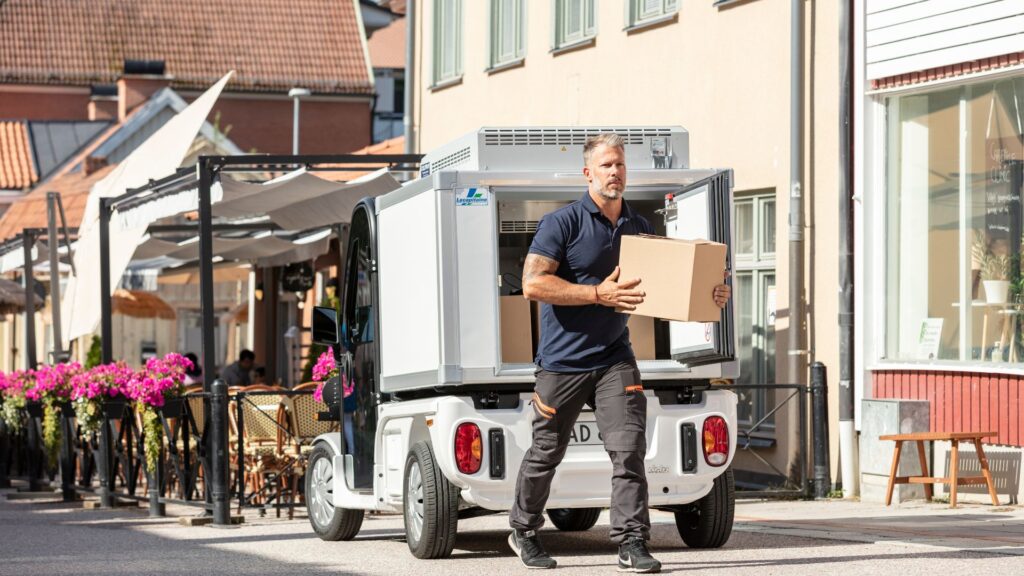 Distribution 9 Pulse 4 är en vit lite lastbil för leverans av paket. Lätt lastbil som är 100% elektrisk. Man som bär ett brunt paket.