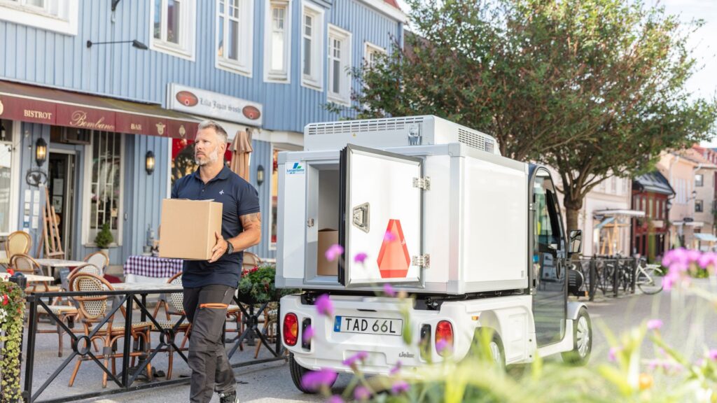 Liten vit lastbil. Man med paket i handen som levererar till ett café.